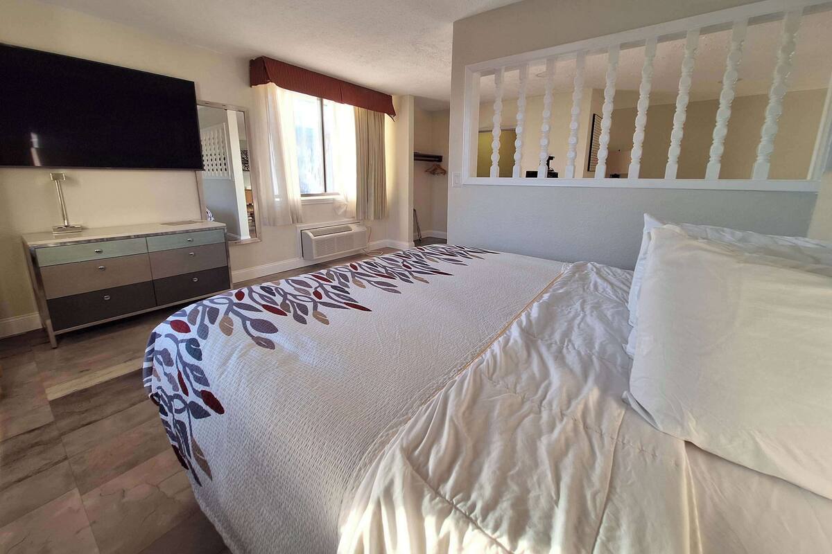 Une chambre avec un grand lit, une commode, un miroir et une fenêtre avec des rideaux.