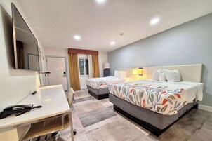 Habitación de hotel con dos camas, un escritorio, un espejo y una ventana con cortinas.