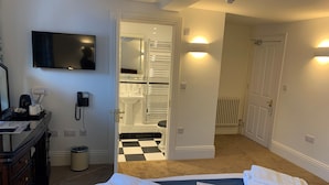 A hotel room with a bed, a desk with a telephone, a television, and a bathroom visible through an open door. - Pilgrims Hotel (Canterbury)