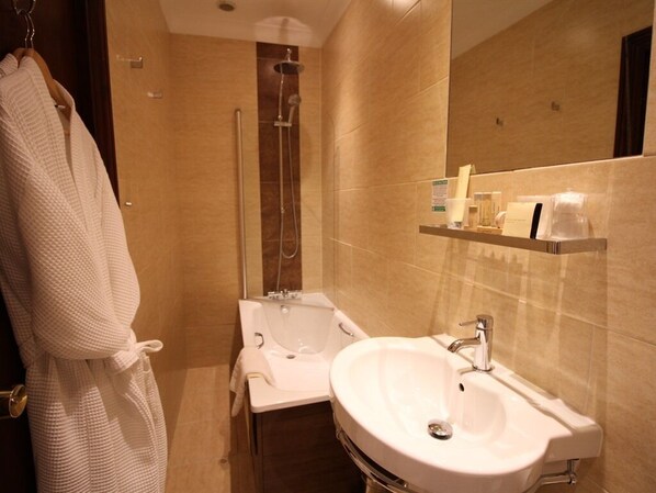 A bathroom with a bathtub, a sink, and a shower. There is a robe hanging on the door. - Pilgrims Hotel (Canterbury)