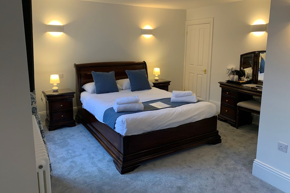 A neatly made bed with pillows, a bedside table with a lamp, and a dresser with a mirror.