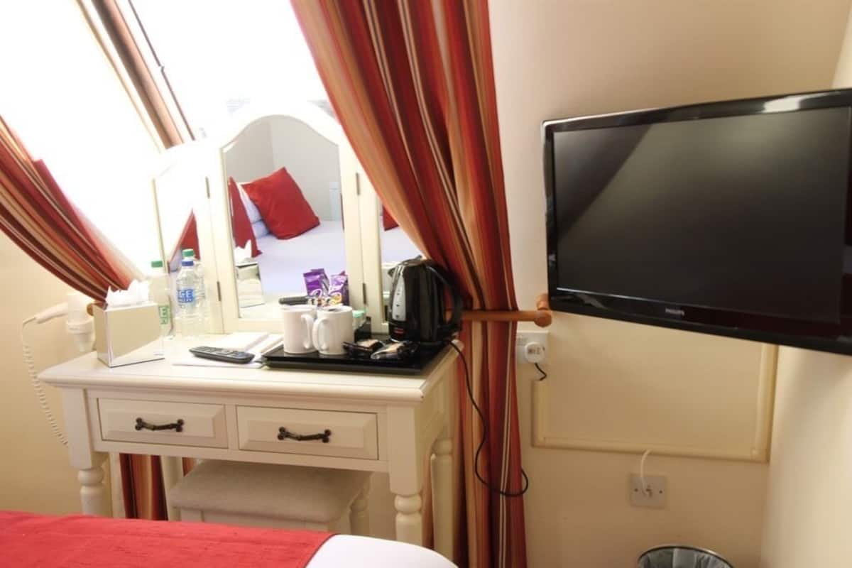 A hotel room with a bed, a desk with a mirror, a television, and a trash can.