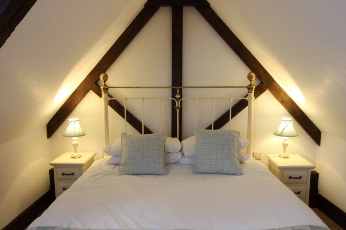 A bedroom with a high ceiling, a bed with white bedding, two bedside tables with lamps, and a wooden ceiling structure.