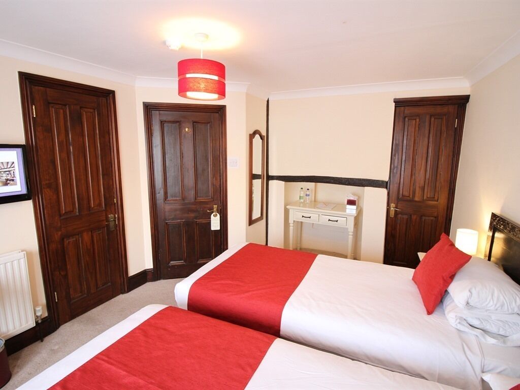 Habitación de hotel con dos camas, un escritorio, un espejo y una lámpara colgante roja.