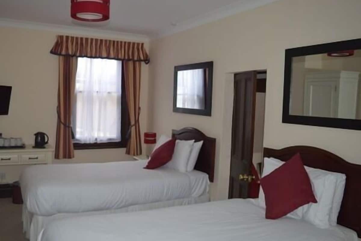 A hotel room with two beds, a desk, a mirror, and a window with curtains.