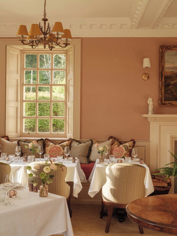 Une salle à manger dotée d’une grande fenêtre, d’un lustre et d’une cheminée.