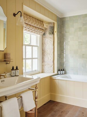 A bathroom with two sinks, a window with a patterned valance, a stone accent wall, and a tiled shower area. - Fortingall (Aberfeldy)