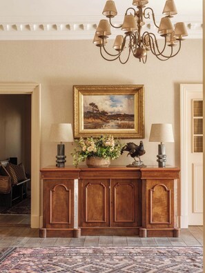 A wooden console table with two lamps, a framed landscape painting, and a decorative bird statue. - Fortingall (Aberfeldy)