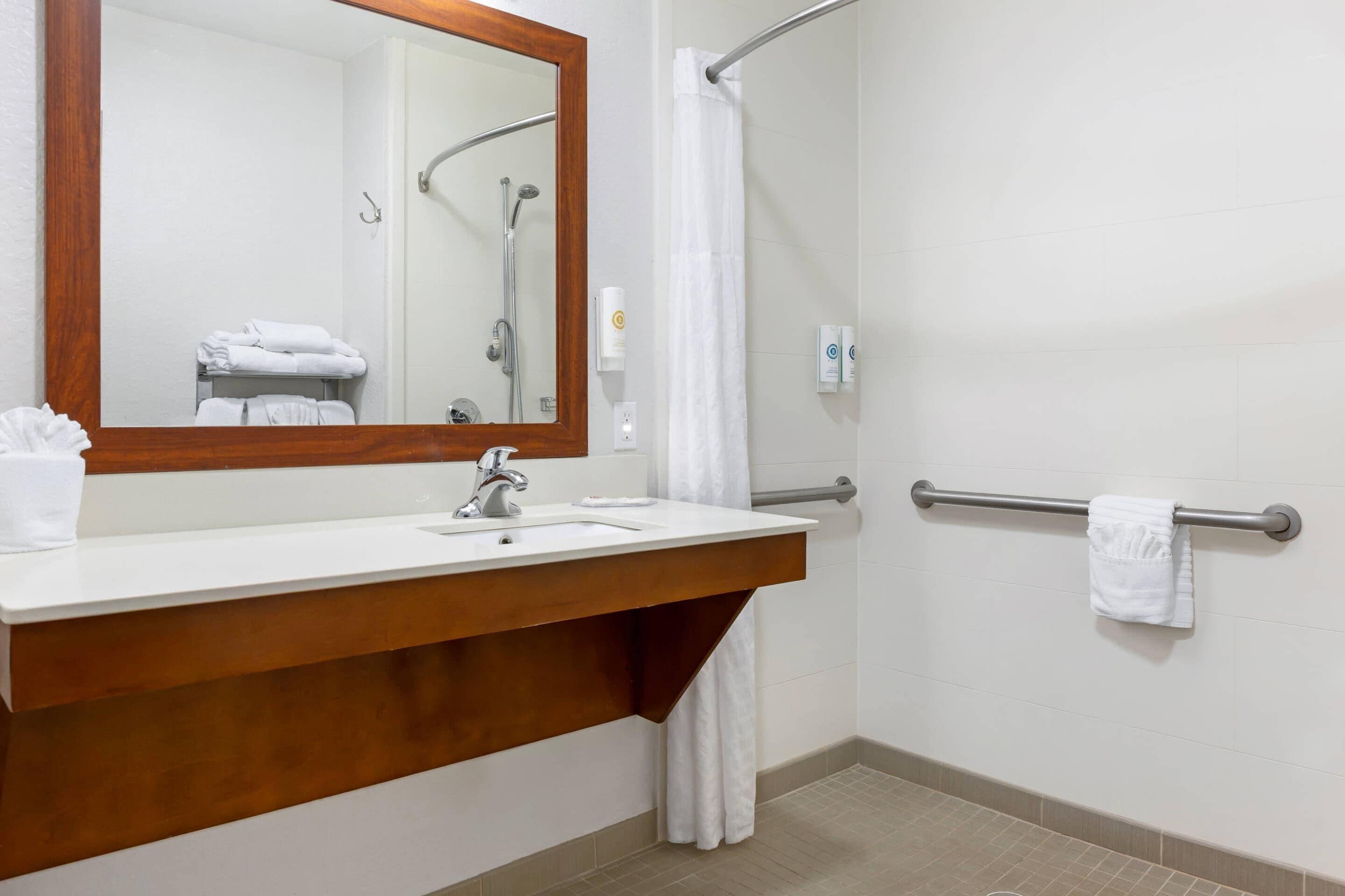 A bathroom with a wooden vanity, a large mirror, a shower with a glass door, and a towel rack.