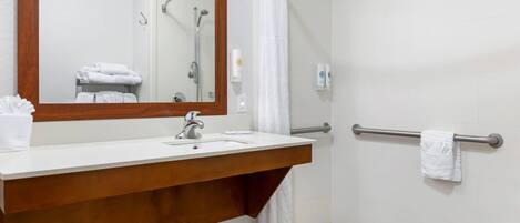 Un baño con tocador de madera, un espejo grande, una ducha con puerta de cristal y un perchero para toallas.