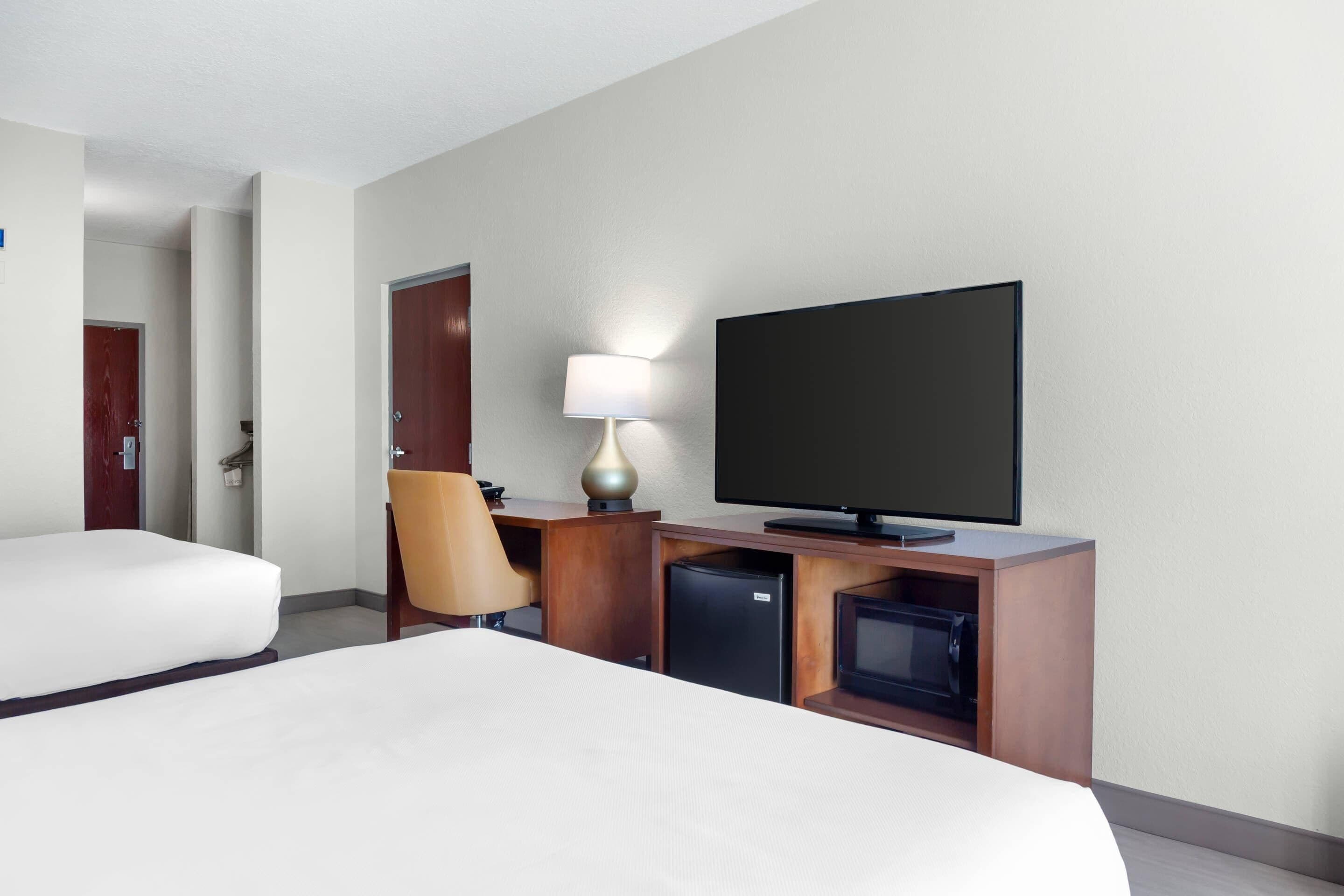 Una habitación de hotel con una cama, un escritorio con televisor, una lámpara y un refrigerador pequeño.