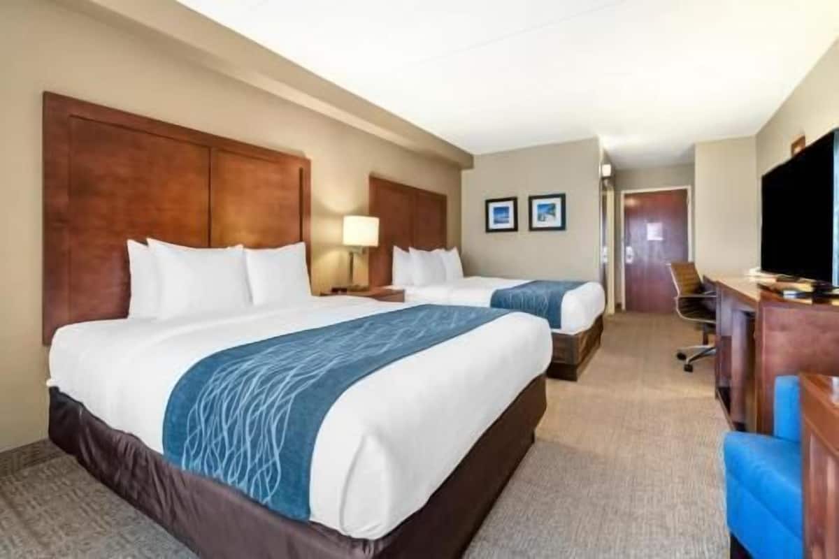 A hotel room with two beds, a desk, a chair, and a television.