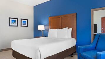 Quarto de hotel com uma cama grande, cabeceira de madeira, parede azul, uma poltrona azul e duas imagens emolduradas na parede.