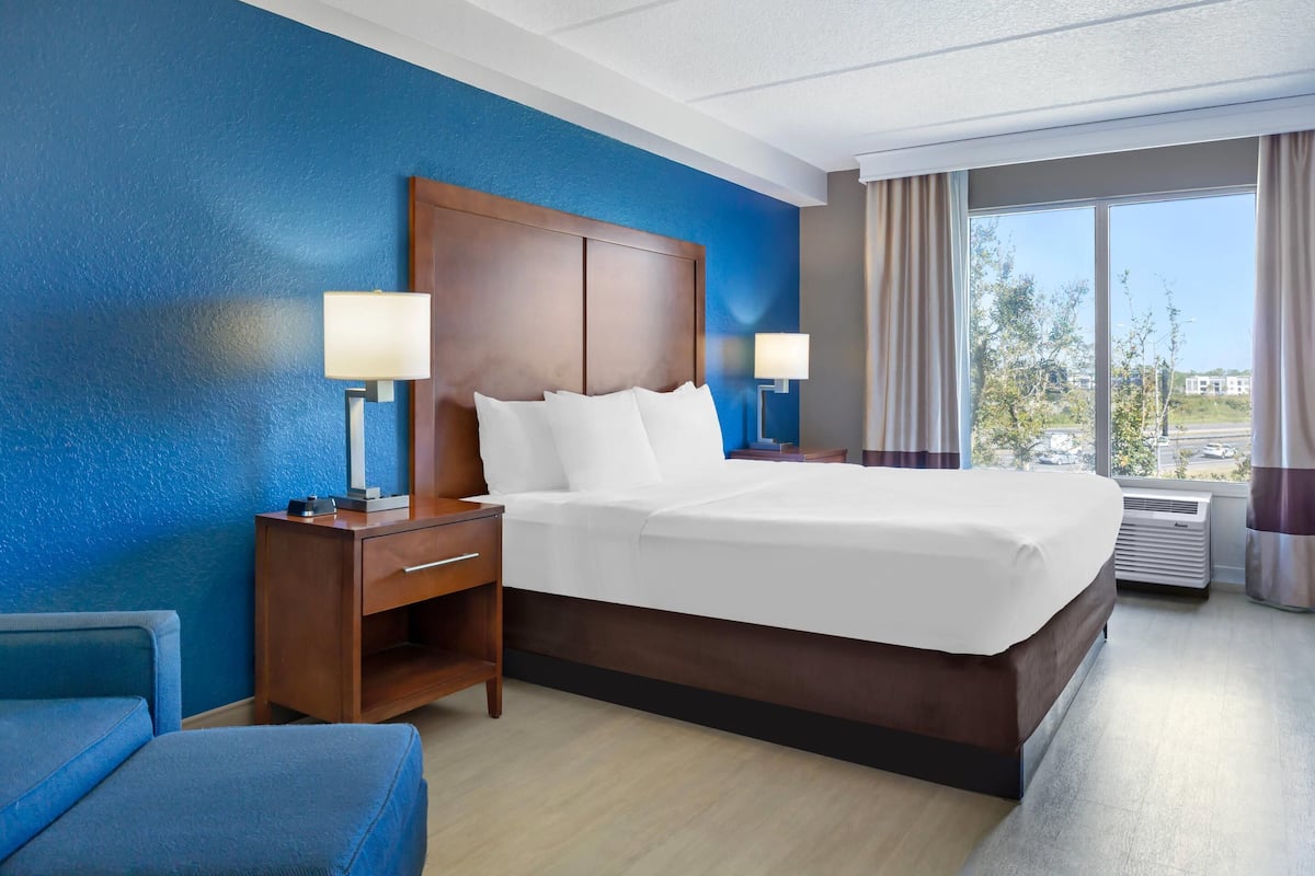 A hotel room with a large bed, a nightstand, a desk, a chair, and a window with curtains.