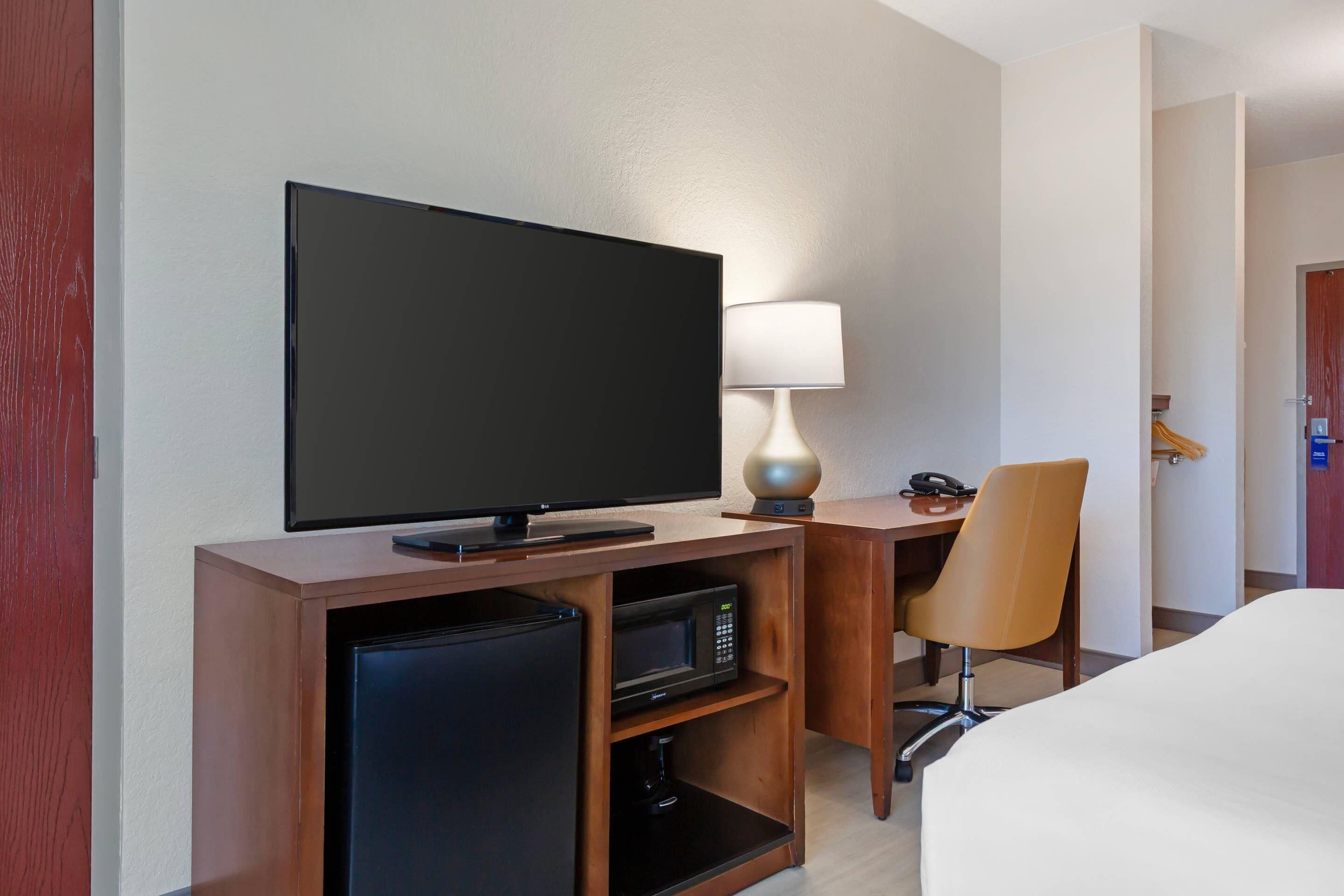 Ein Hotelzimmer mit Flachbildfernseher, Lampe, Mikrowelle, Minikühlschrank und einem Sessel.