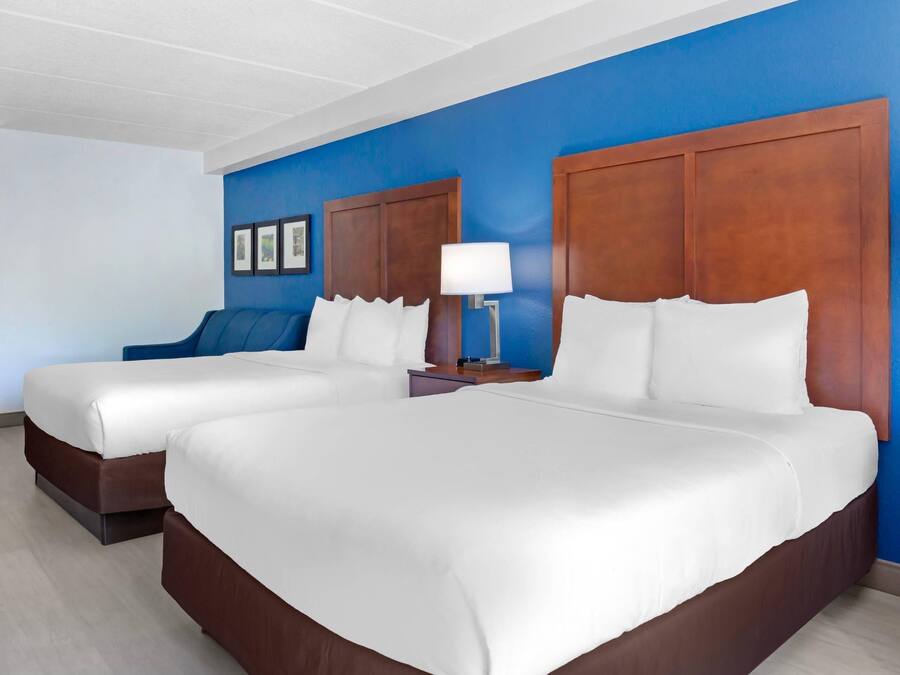 A hotel room with two beds, a blue accent wall, and a wooden headboard.