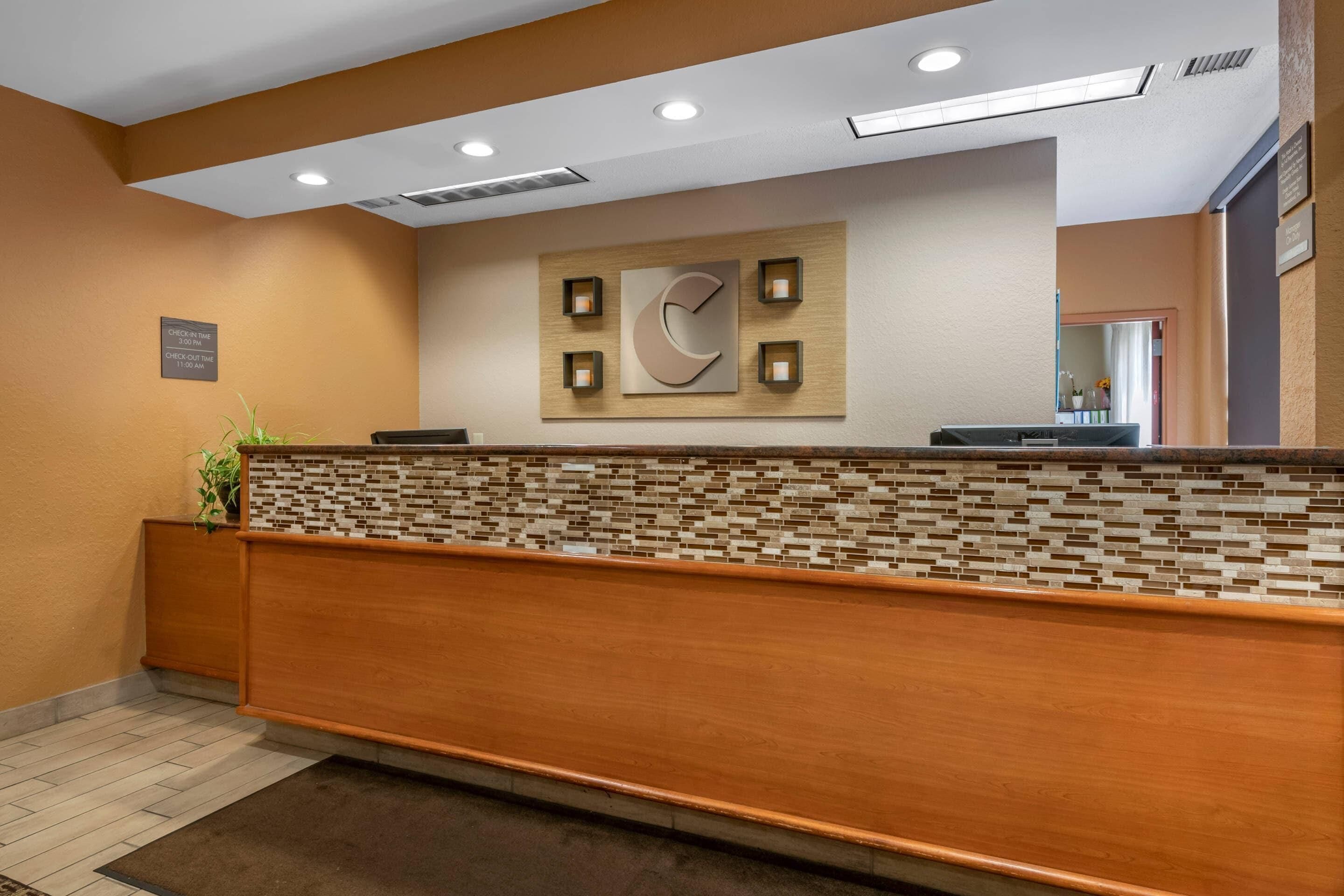 Bancada de recepção com revestimento de mosaicos, um relógio e uma placa indicando os horários de check-in.