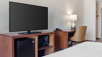 A hotel room with a flat-screen TV, a desk with a lamp, a microwave, a refrigerator, and a bed.