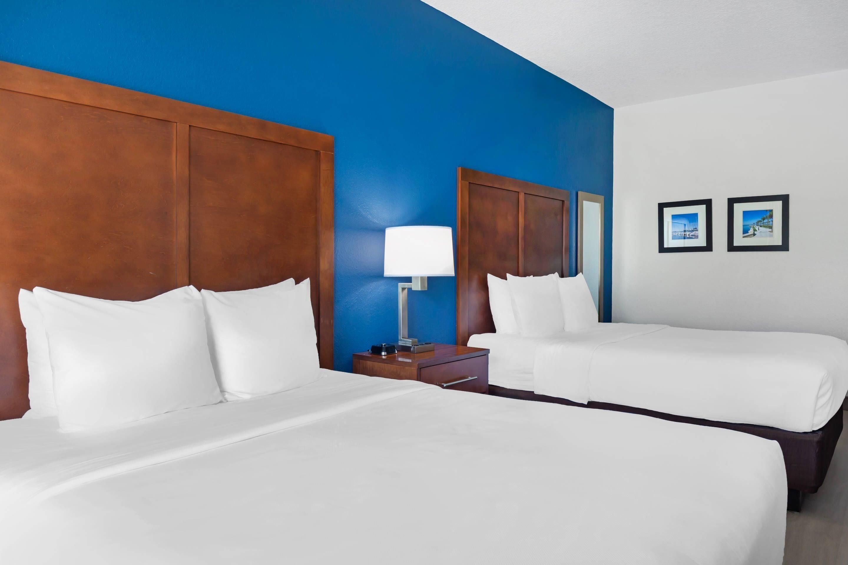 A hotel room with two beds, a nightstand with a lamp, and two framed pictures on the wall.