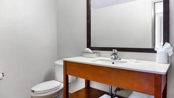 A bathroom with a white toilet, a wooden vanity with a mirror, and a sink.