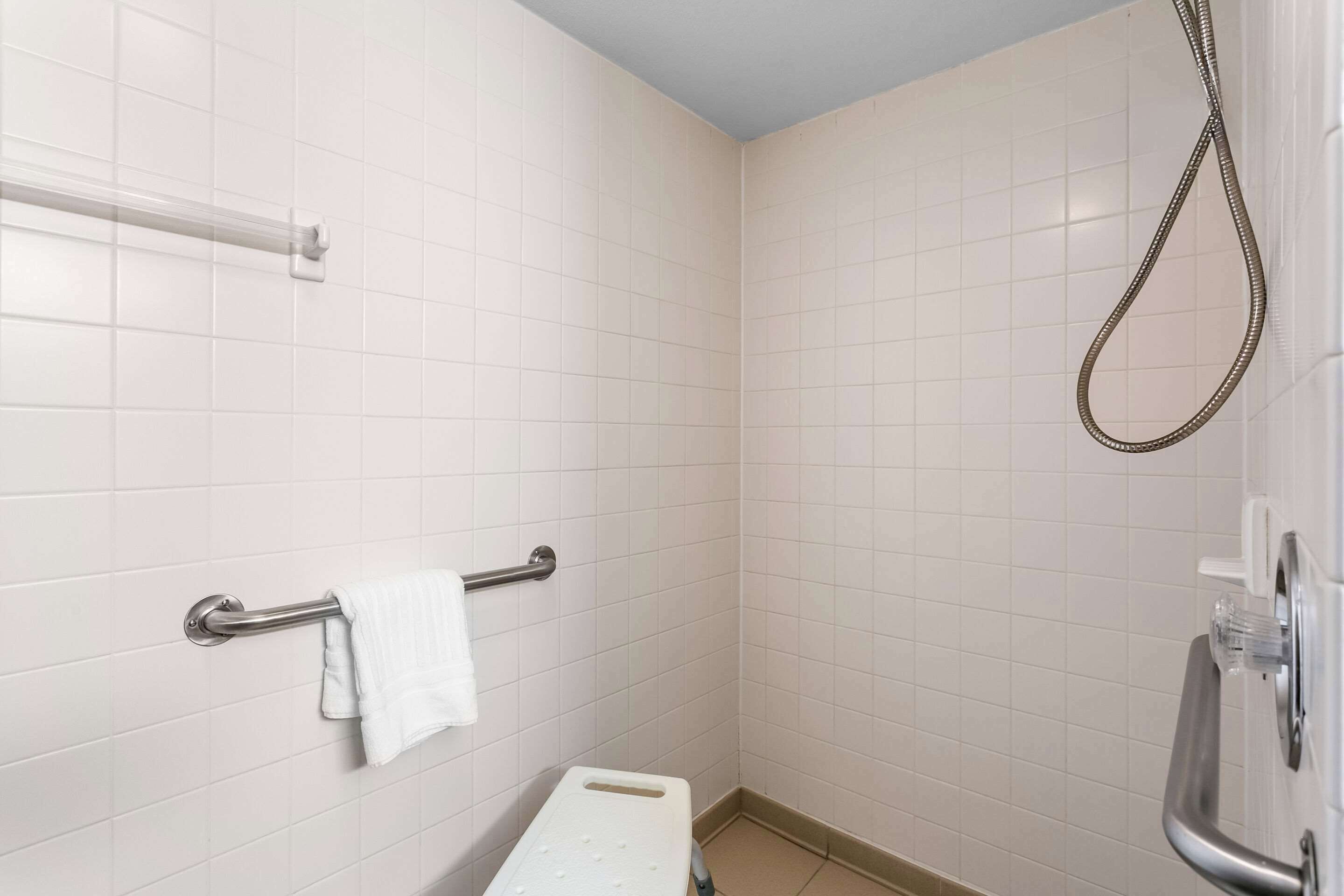 A small, tiled bathroom with a shower, a grab bar, and a towel rack.