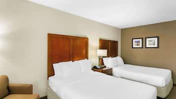 A hotel room with two beds, a wooden headboard, a bedside table with a lamp, and two framed pictures on the wall.