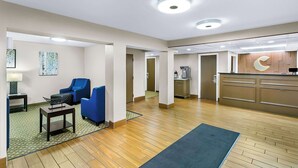 Vestíbulo de hotel con mostrador de recepción, zona de estar azulada y kitchenette.