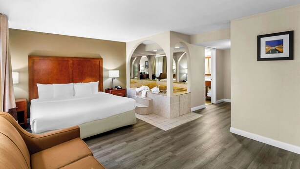 Habitación de hotel con una cama grande, una zona de estar, un baño con espejo y un cuadro en la pared.