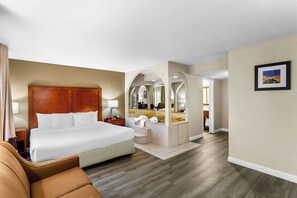 A hotel room with a large bed, a sitting area, a bathroom with a mirror, and a picture on the wall. - Comfort Inn Red Horse Frederick (Frederick)