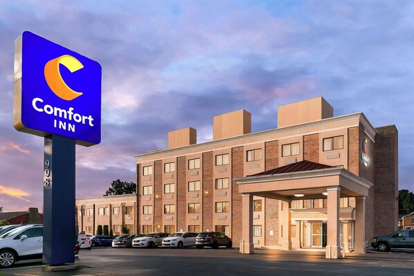 Un hôtel Comfort Inn, reconnaissable à son enseigne bien visible, son bâtiment en briques et son parking où sont stationnées plusieurs voitures.