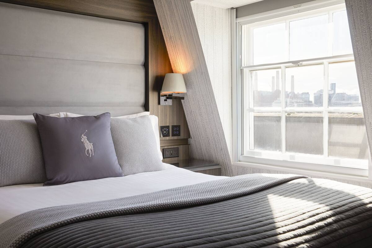 A modern hotel room with a large bed, a city view, and a nightstand with a lamp.