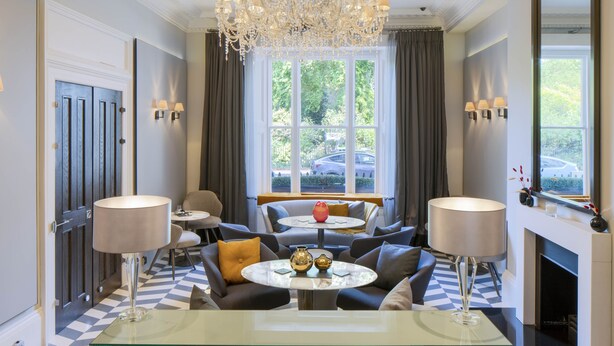A modern living room with a chandelier, a fireplace, and a large window with a view of the outside. - Eccleston Square Hotel (London)
