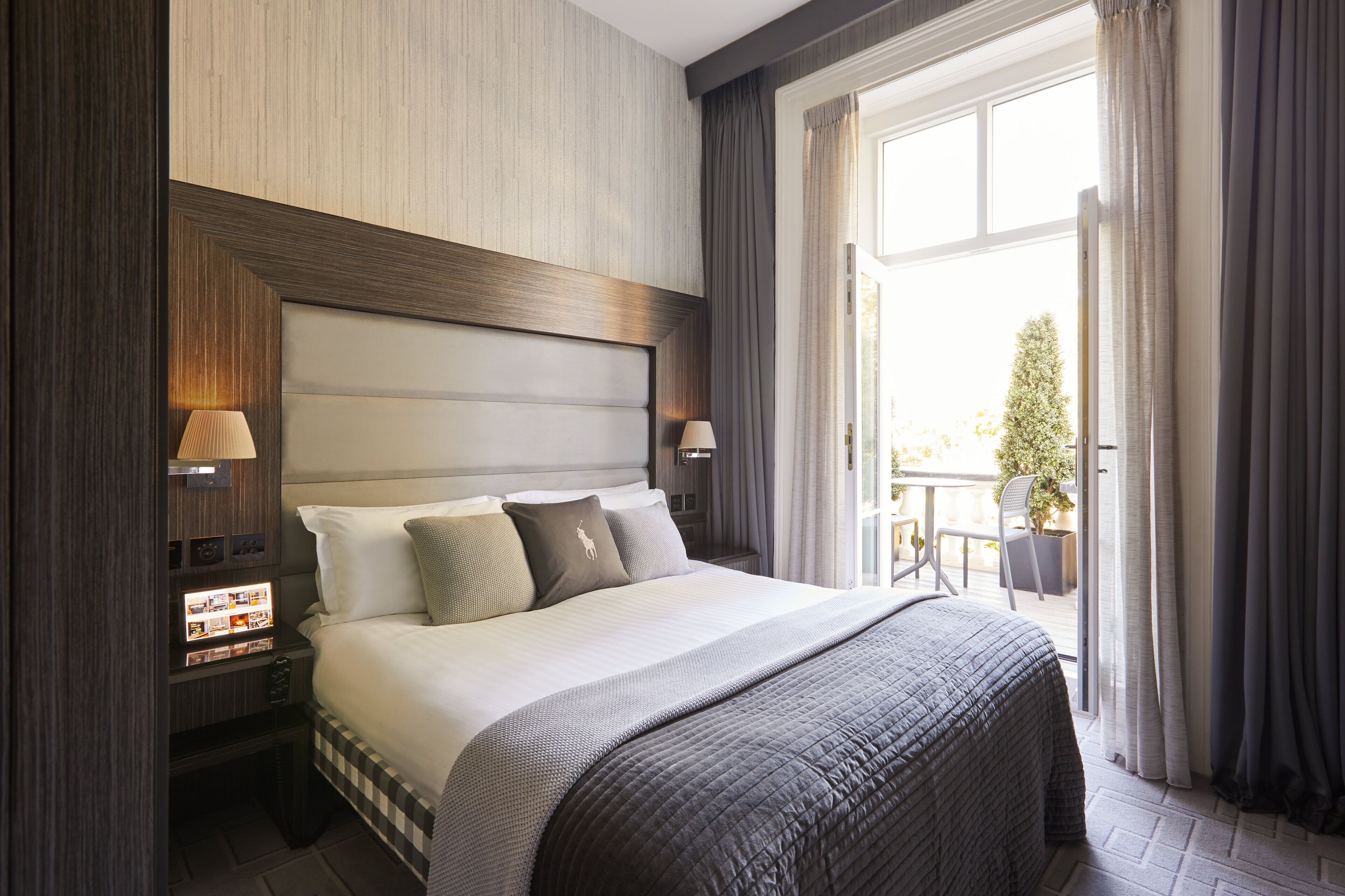 Une chambre d’hôtel avec un grand lit, deux lampes de chevet, une table de chevet ornée d’un photomontage et une vue sur l’extérieur grâce à une grande fenêtre.