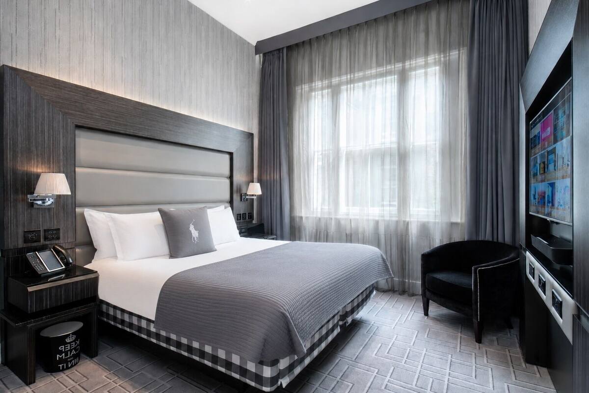 A modern hotel room with a large bed, a flat-screen TV, a desk with a phone, and a chair.