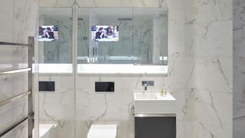 A modern bathroom with a glass partition, a white toilet, a sink with a mirror, and a television screen.