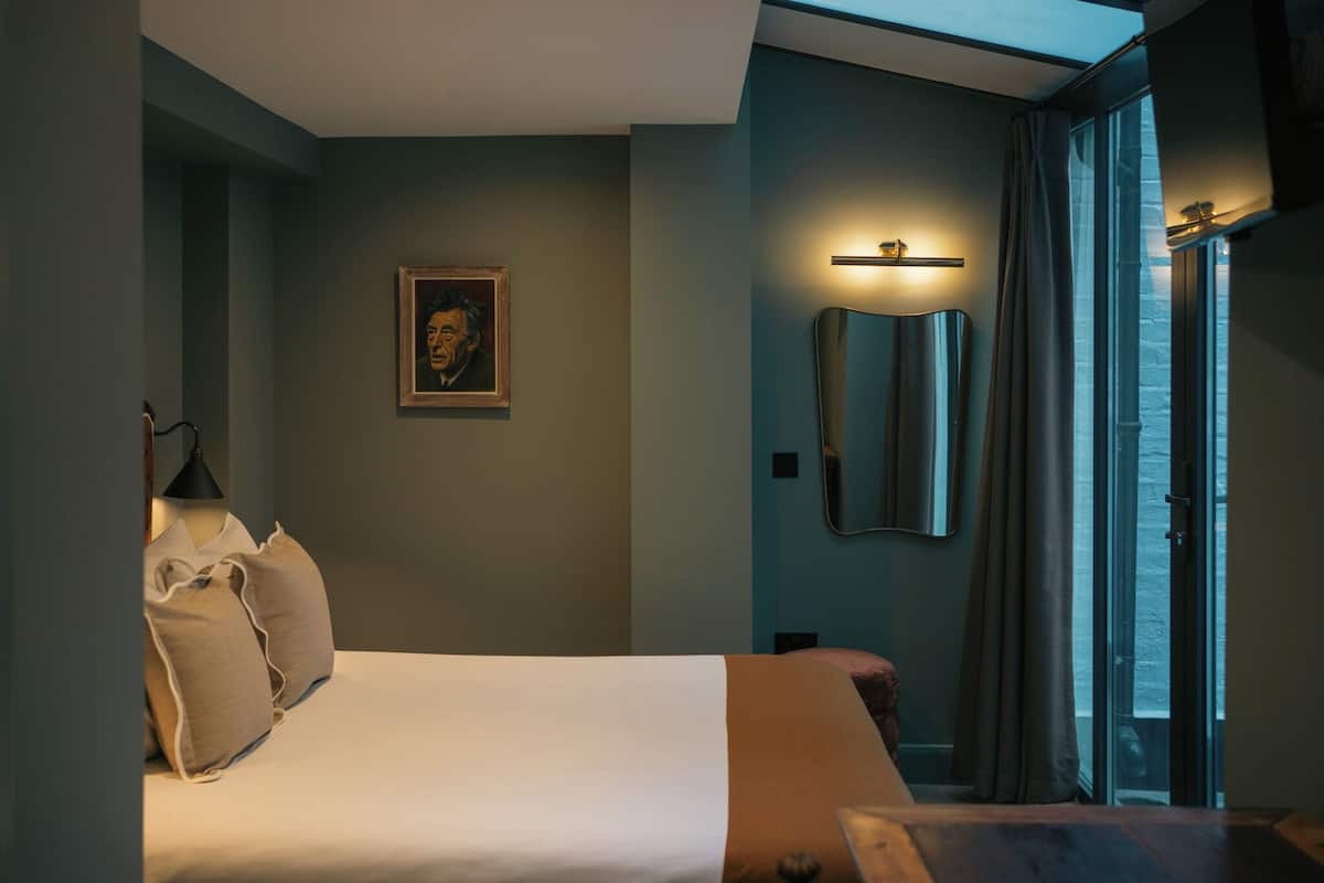 A bedroom with a bed, pillows, a framed picture, a mirror, and a sliding door to a balcony.