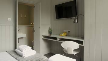 A modern hotel room with a large bed, a desk, a TV, and a bathroom visible through an open door.