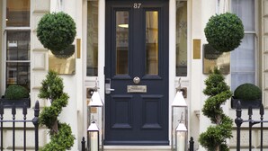 A black double door with the number 87, flanked by two small potted trees and two lit lanterns. - Georgian House Hotel (London)