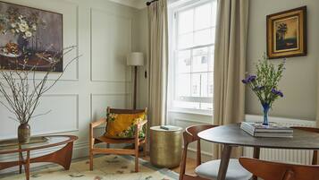 Un comedor con una mesa de madera, sillas, un jarrón con flores, un cuadro en la pared y una ventana con cortinas.