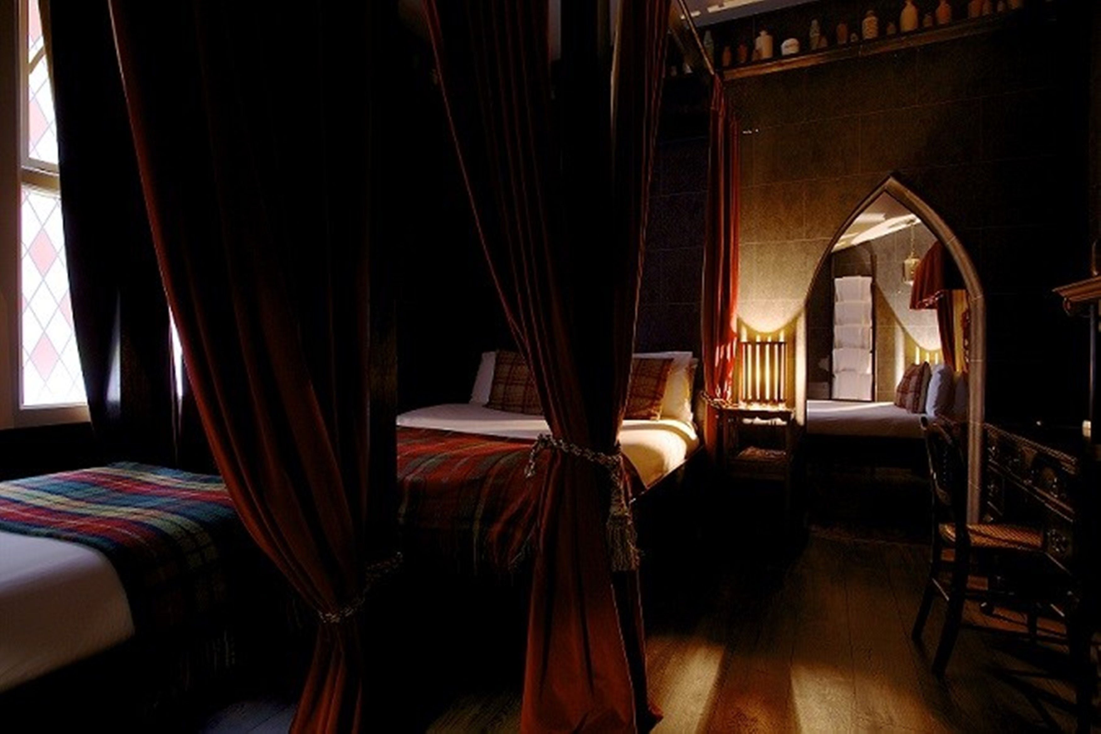 A bedroom with a four-poster bed, a separate sitting area with a chair, and a small table.