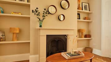 A living room with a fireplace, shelves with books and decorative items, and a round table with a vase and books.