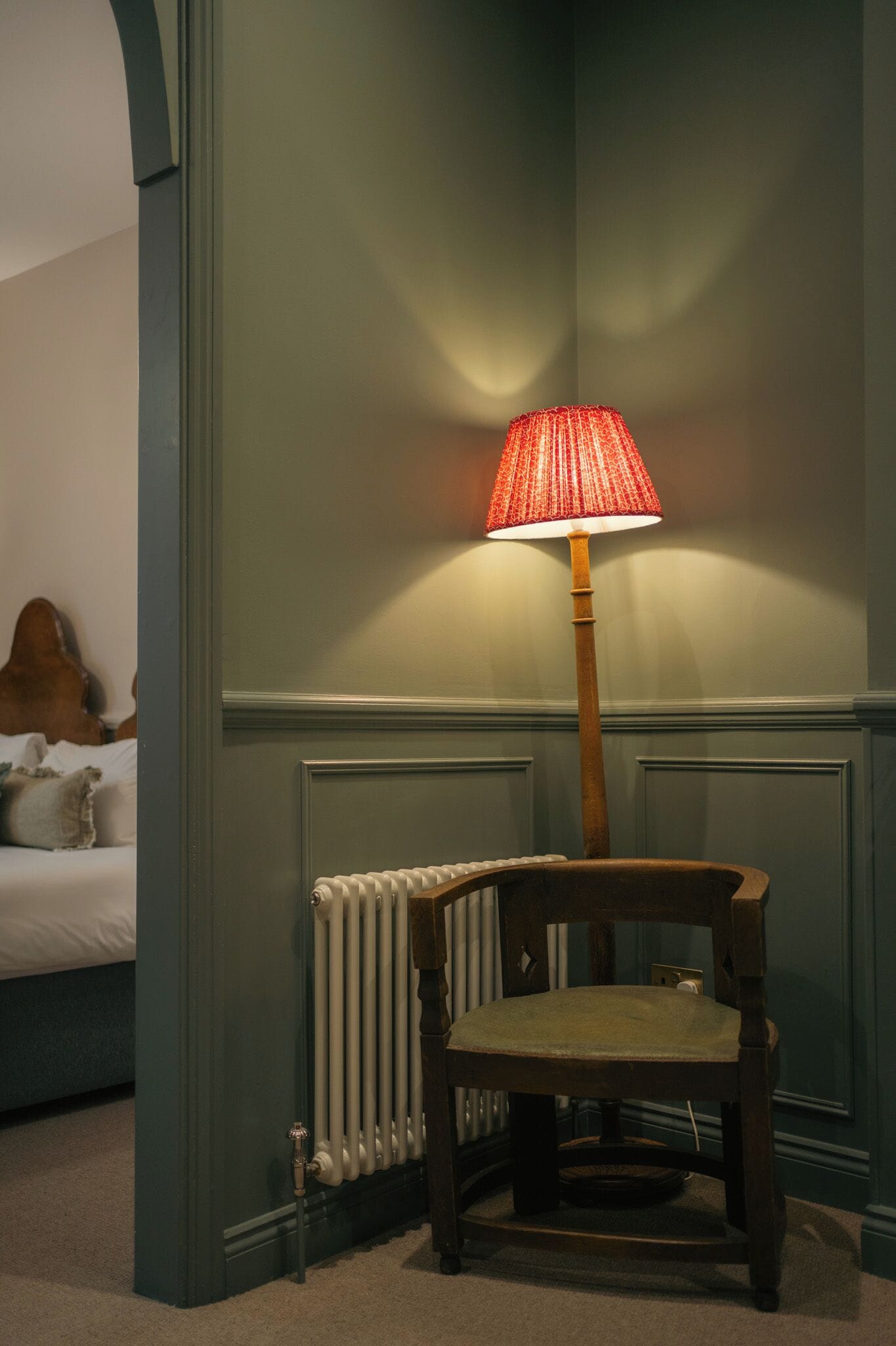 Et værelse med en radiator, en træstol og en lampe med rød skærm.