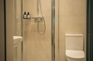 A bathroom with a glass-enclosed shower, a toilet, and a shelf with two bottles.