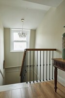 Eine Holztreppe mit schwarzer Handlauf und einer Leuchte darüber.