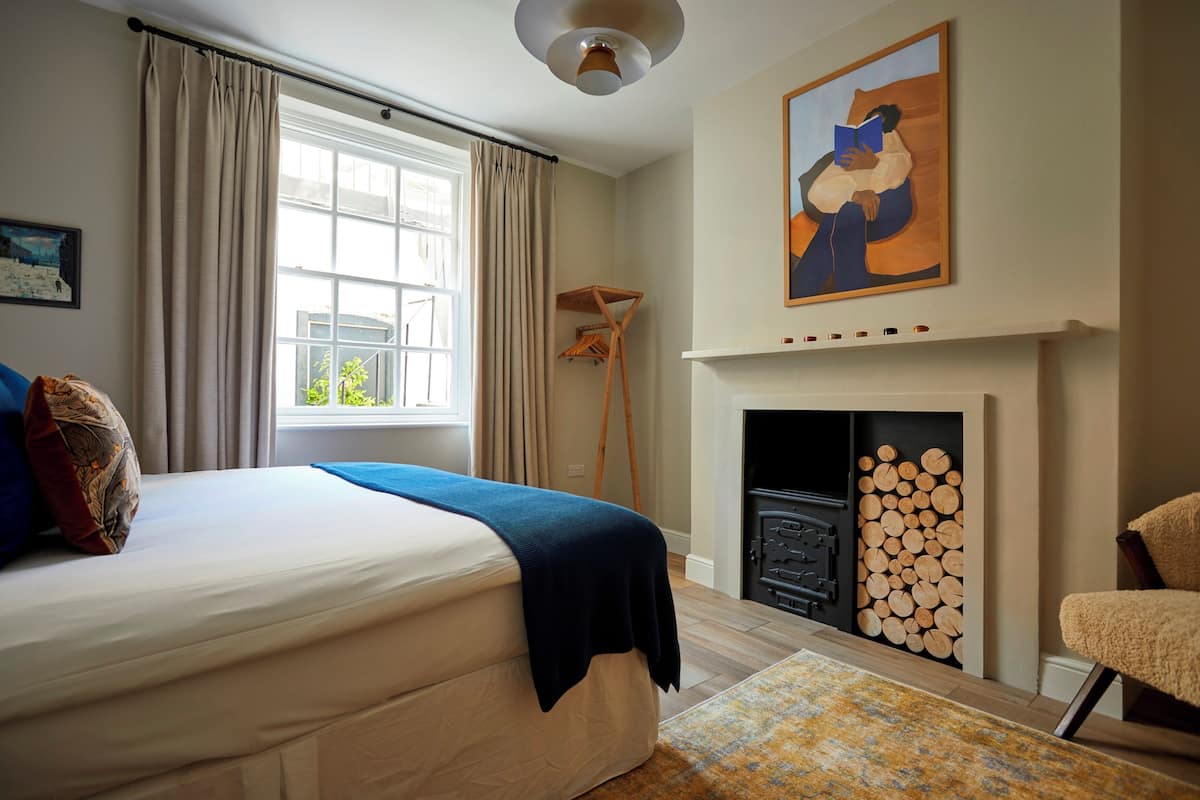 A bedroom with a bed, a fireplace, a window with curtains, and a painting on the wall.