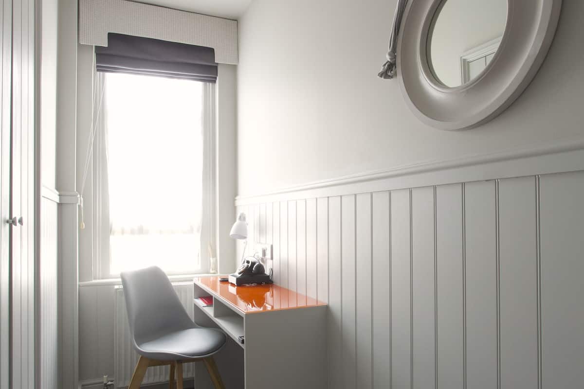 A compact room with a desk, chair, and a round mirror on the wall.