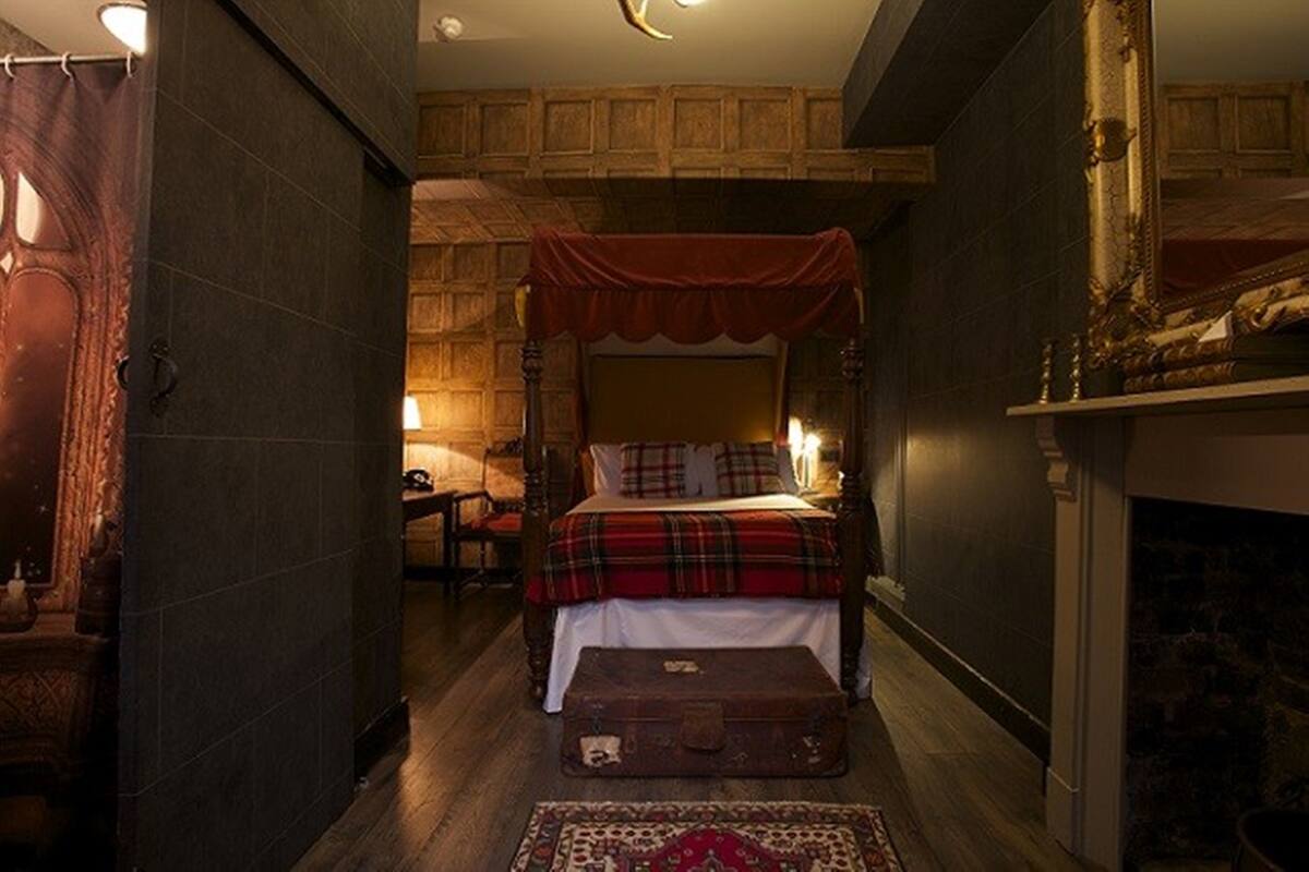 A traditional room with a four-poster bed, a fireplace, and a rustic wooden floor.