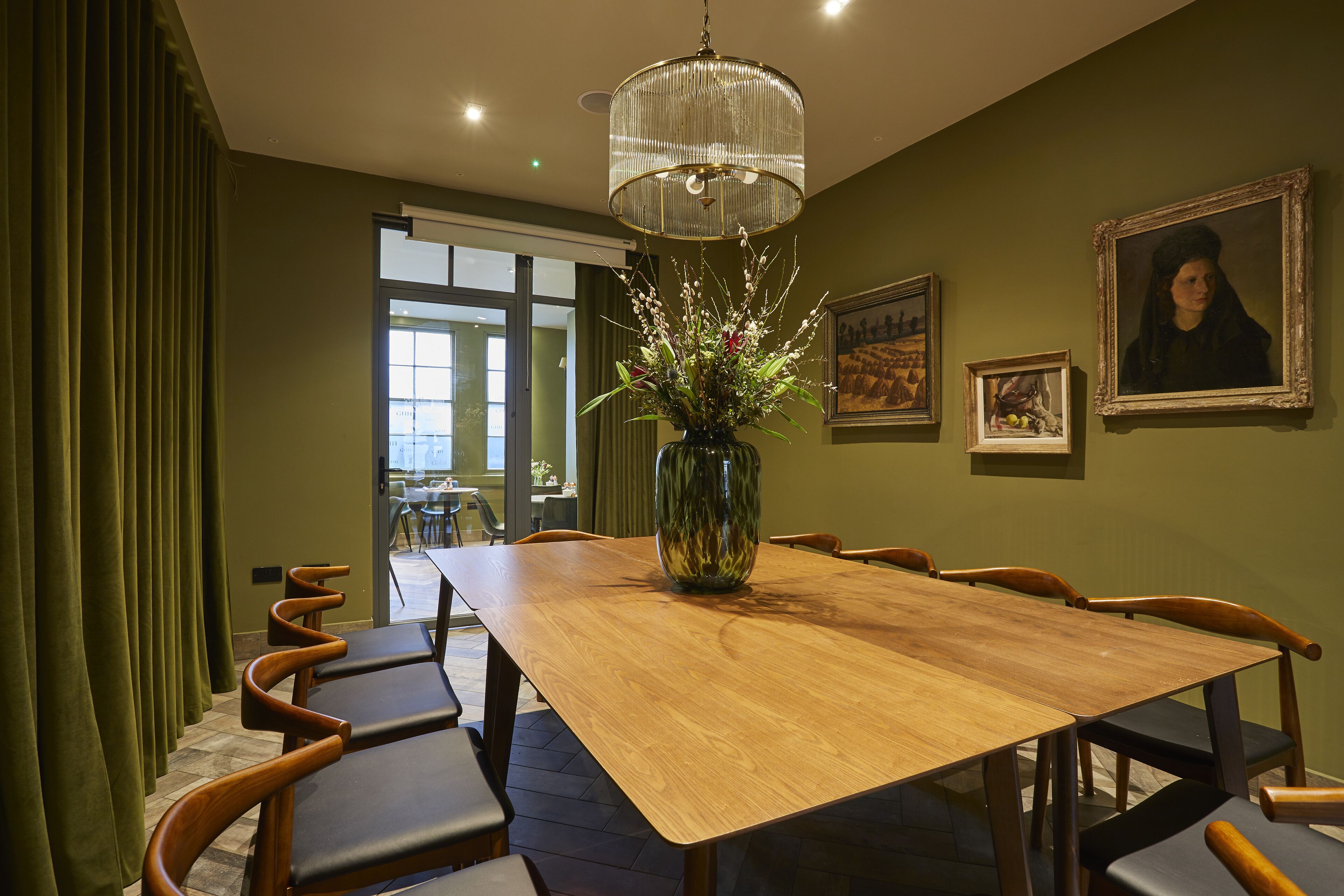 A dining area with a wooden table, chairs, a vase with flowers, and framed artwork on the wall.