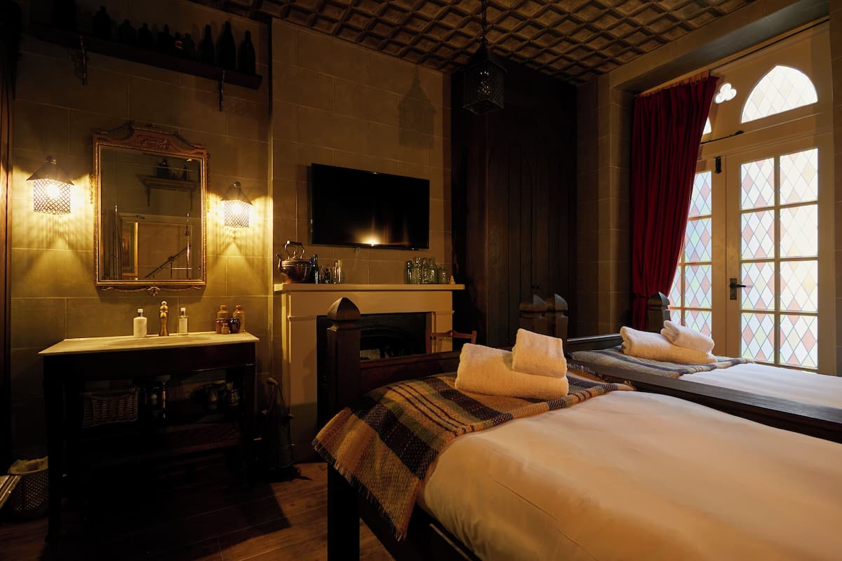 A hotel room with a large bed, a fireplace, a TV, and a window with a red curtain.