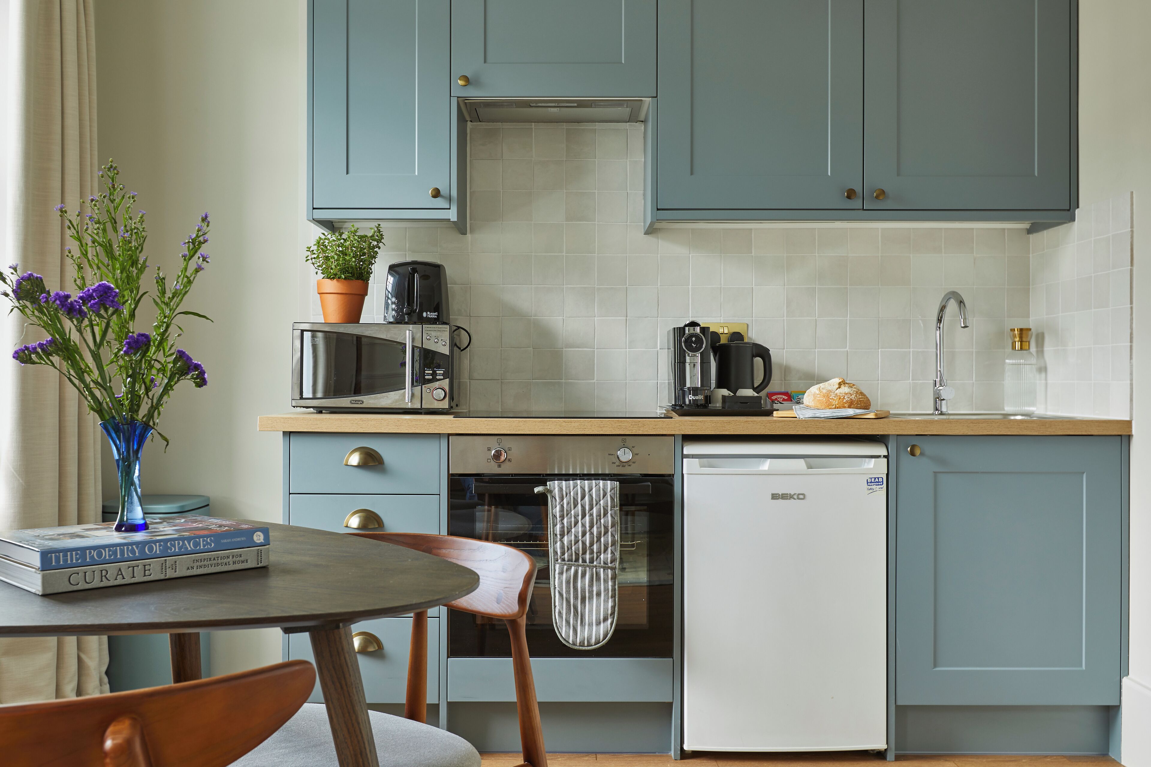 A kitchen with teal cabinets, a microwave, a coffee maker, a toaster, a sink, and a dishwasher.